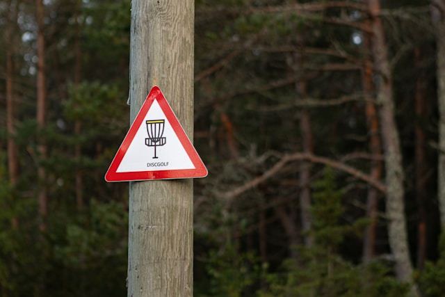 A pole with a disc golf basket sign sitting on it