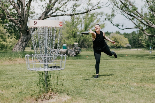 A woman throwing into a disc golf basket