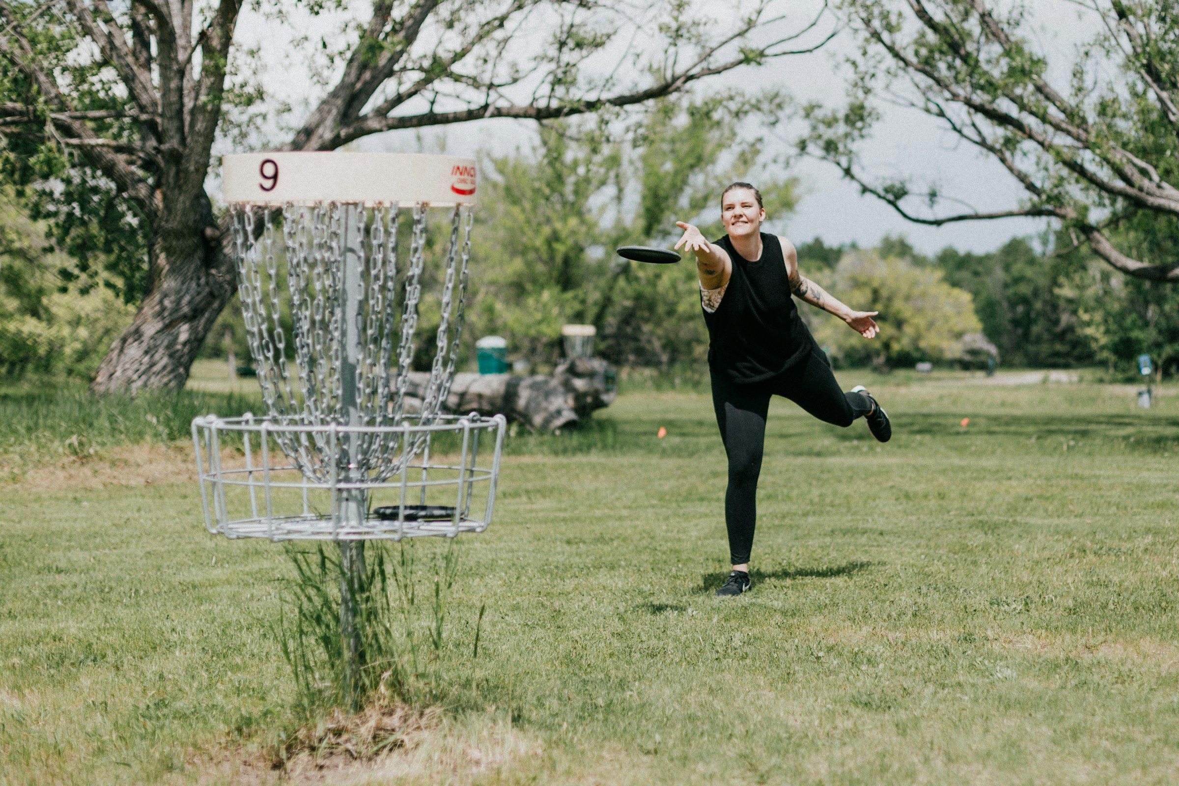 A woman throwing into a disc golf basket