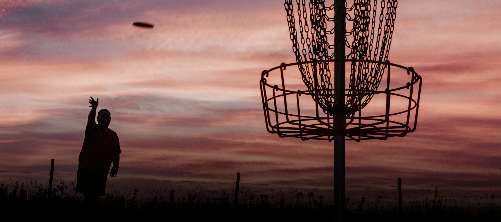 A disc golf basket at sunset and the shadow of a man playing.