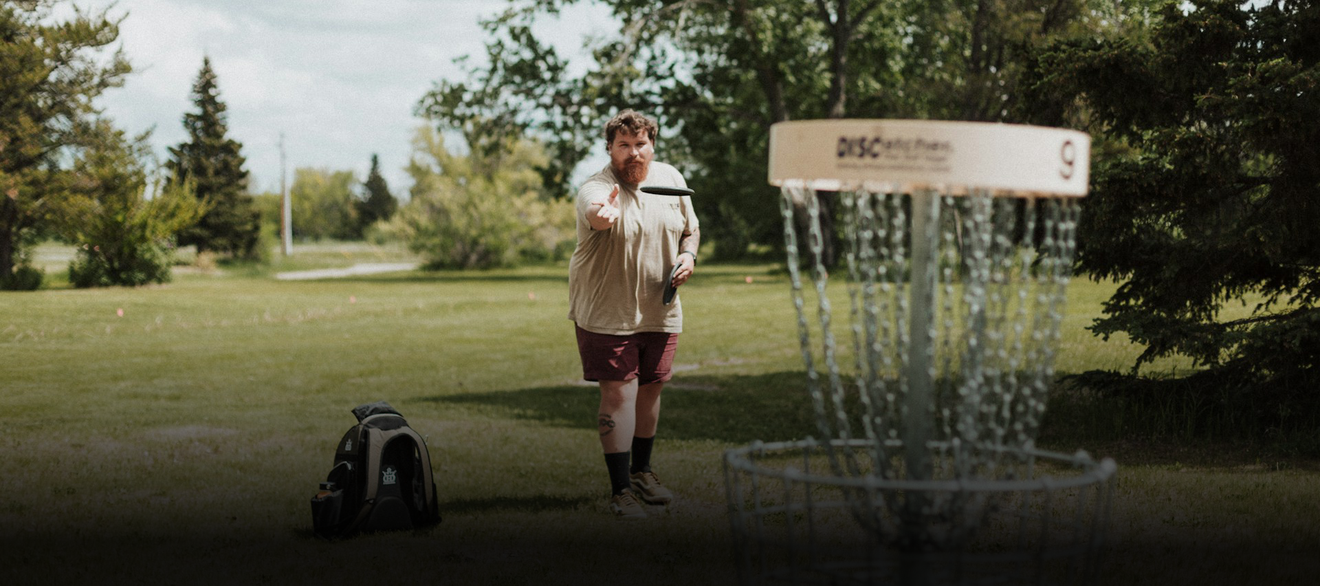 A man playing disc golf in an open field throwing the disc to a basket.